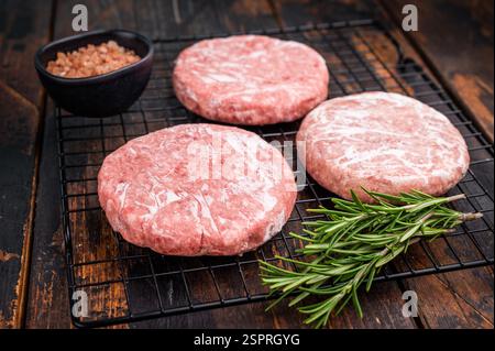 Gefrorene Fleischpasteten, bereit zum Grillen, Forcemeat von Schwein und Rindfleisch für Burger. Hölzerner Hintergrund. Draufsicht. Stockfoto