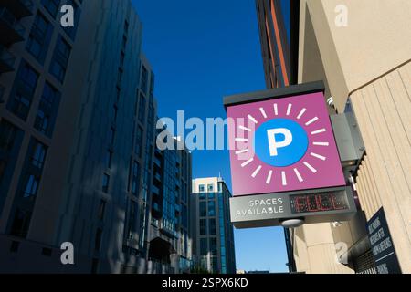 Digitale Parkplatzschilder in violetten und blauen Farbtönen, die sich an modernen Wohn- und Geschäftsgebäuden abheben. Nahaufnahme Stockfoto