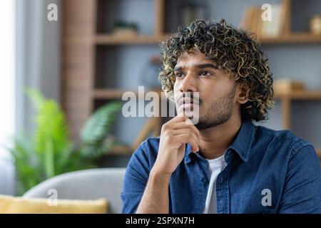 Ernsthaft denkender Mann aus der Nähe, blickt zu Hause aus dem Fenster, nachdenklich im Wohnzimmer, sitzt auf der Couch. Stockfoto