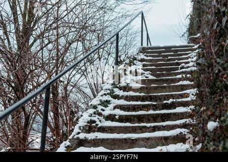 Gefährliche und rutschige Treppen, die mit Schnee und Moos bedeckt sind. Der Schutz der Führungsschiene ist links sichtbar. Stockfoto
