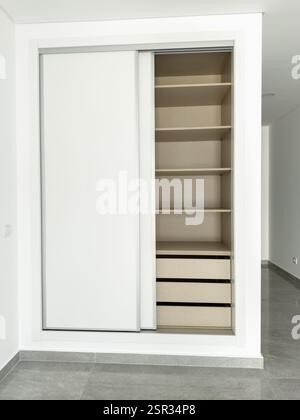 Moderner Einbauschrank mit weißen Schiebetüren, offen für Regale und Schubladen. Stockfoto