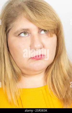 Nahporträt einer Reifen Frau mit blonden Haaren und grünen Augen, die ein gelbes Oberteil trägt. Stockfoto