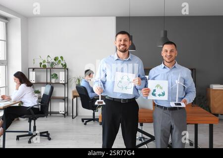 Männliche Ingenieure mit Windturbinenmodellen und Recycling-Schildern im Büro Stockfoto