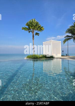 Kristallklares Wasser spiegelt die Schönheit Thailands wider, wo ein ruhiger Pool auf üppige Palmen trifft. Eine charmante Cabana lädt zum Entspannen ein und ergänzt die perfekte tropische Umgebung. Stockfoto