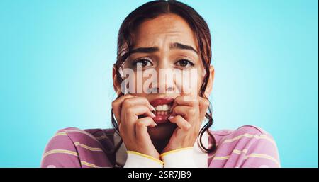 Frau, Porträt und beißende Nägel mit Angst im Studio wegen Sorge, Angst oder Panik mit Druck. Raum, Mädchen und nervös mit Stress auf blauem Hintergrund Stockfoto