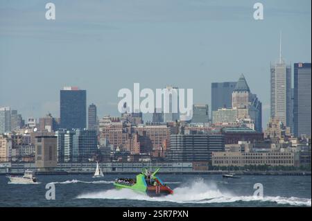 Die Skyline von New York City erstrahlt in der Ferne, während ein Boot das Wasser überquert, voll von Touristen, die ein Sightseeing-Abenteuer genießen. Stockfoto