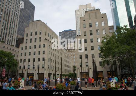 Art déco-Wolkenkratzer erheben sich über einem plaza mit einer zentralen Skulptur. Eine geschäftige Szene im Herzen von New York City, Rockefeller Center in Midtown M Stockfoto