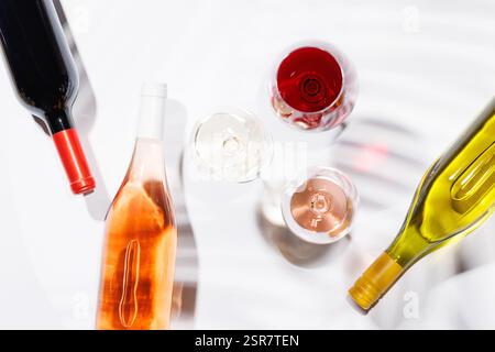 Drei Weingläser gefüllt mit Rot-, weiß- und Rosenwein, anmutig auf einem hellen, minimalistischen Hintergrund. Eine lebendige Darstellung der Vielfalt der Weine Stockfoto
