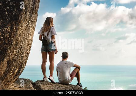 Ein paar junge Touristen sitzen und entspannen auf einem großen Felsen vor der Meeresbucht mit toller Aussicht. Tropisches Wochenendkonzept Stockfoto