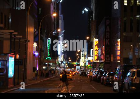 In New York City in Manhattan navigiert ein Mann in schwarzer Jacke und Jeans, der über die Schulter geschlungen ist, durch die hektischen Menschenmassen und Neonlichter von Ti Stockfoto
