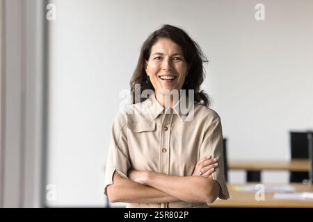 Reife Frau, die selbstbewusst im Büro steht und die Arme überkreuzt Stockfoto