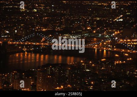 New York, Manhattan, taucht aus der Dunkelheit hervor, eine schillernde Farbenpracht über den Wolkenkratzern. Die legendäre Brooklyn Bridge erstreckt sich über die Stockfoto