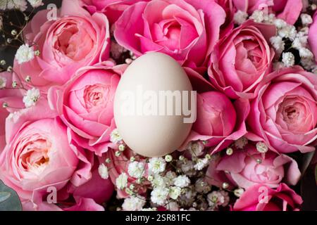 Ein braunes Hühnerei liegt auf einem Strauß rosa Strauchrosen, Osterfeiertag Stockfoto