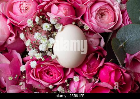 Ein braunes Hühnerei liegt auf einem Strauß rosa Strauchrosen, Osterfeiertag Stockfoto
