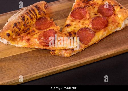 Zwei Scheiben Peperoni Pizza auf einem hölzernen Schneidebrett mit geschmolzenem Käse und knuspriger Kruste Stockfoto