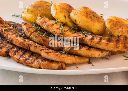 Nahaufnahme von geschnittenen gegrillten Schweinekoteletts mit knusprigen Kartoffeln und frischer Thymian-Garnele Stockfoto