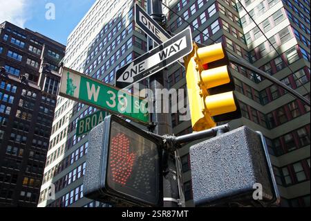 Eine Verkehrsampel und Straßenschilder hängen an einem Pfosten im belebten New York, Manhattan. Die Signale stehen Wächter vor einem hochaufragenden Wolkenkratzer, der t säumt Stockfoto