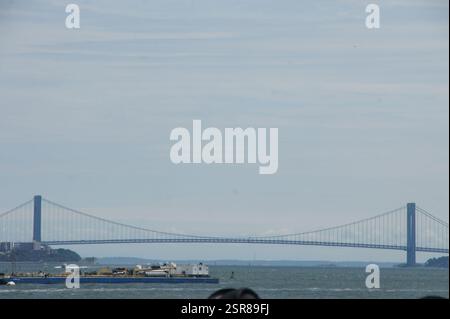 Eine malerische Szene des New Yorker Hafens entfaltet sich, mit einem einsamen Boot, das ruhig im Wasser wippt, das von der majestätischen Verrazzano-Narrows Bridge-Straße gedämpft wird Stockfoto