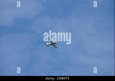 In New York, Manhattan, schwebt ein kleines weißes Flugzeug durch einen hellblauen Himmel, der von geschwollenen Wolken gesäumt ist. Das einmotorige Propellerflugzeug, wahrscheinlich ein CE Stockfoto