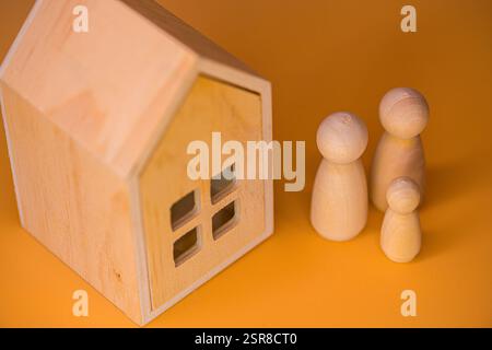 Holzfiguren, die einer Familie ähneln, neben einem kleinen Holzhausmodell, das Heim und Zweisamkeit symbolisiert Stockfoto