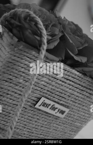 Eine atemberaubende Schwarz-weiß-Nahaufnahme von frisch gepflückten roten Rosen in einer rustikalen Jutebox. Die zeitlosen Schwarzweißtöne unterstreichen die zarte Schönheit Stockfoto