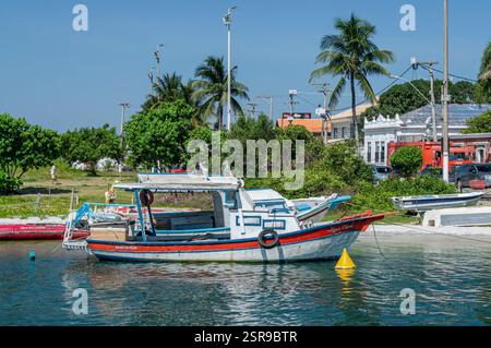 Kleine hölzerne Fischerboote vor Anker an der Nordostküste des Itajuru-Kanals mit grüner Vegetation und Kolonialgebäuden unter dem blauen Himmel am Sommernachmittag. Stockfoto