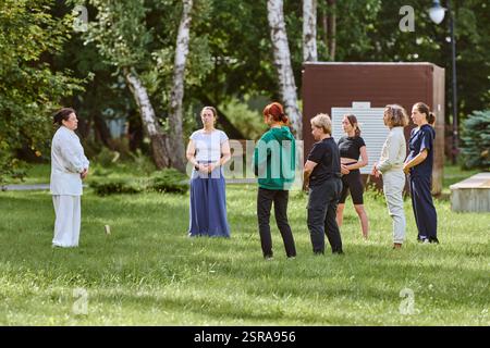 Gruppe von sechs Erwachsenen, die Qigong im Freien üben. Zu den Teilnehmern zählen junge und reife Erwachsene verschiedener ethnischer Zugehörigkeit. Frauen und Männer tragen lässige Atts Stockfoto