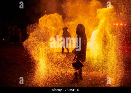 Silhouette zweier Feuerkünstler mit funkelndem Feuerwehrpersonal, das am Nachthimmel ausbricht und die Energie und Kunst der Feuermanipulation während eines Outdours zeigt Stockfoto