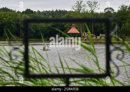 Friedliche Seeszene mit einem Pavillon mit rotem Dach, Spielplatz und üppigem Grün, umgeben von Gras und reflektierendem, ruhigem Wasser Stockfoto