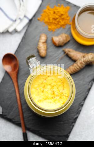 Köstlicher Kurkuma-Latte mit Honig, Pulver und Rhizomen auf grauem Tisch, flach gelegen Stockfoto