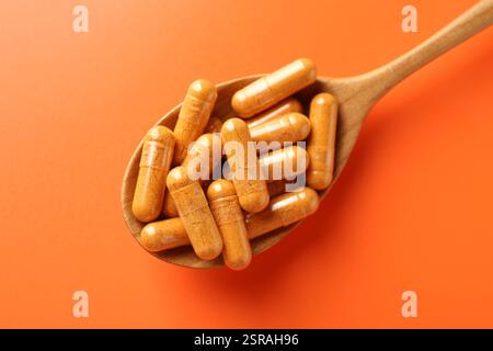 Kurkuma-Kapseln in Holzlöffel auf orangem Hintergrund, Draufsicht Stockfoto