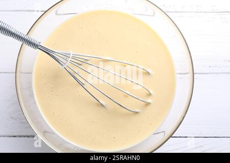 Schneebesen und eine Schüssel Teig auf weißem Holztisch, Draufsicht Stockfoto