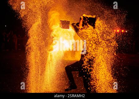 Silhouette zweier Feuerkünstler mit funkelndem Feuerwehrpersonal, das am Nachthimmel ausbricht und die Energie und Kunst der Feuermanipulation während eines Outdours zeigt Stockfoto