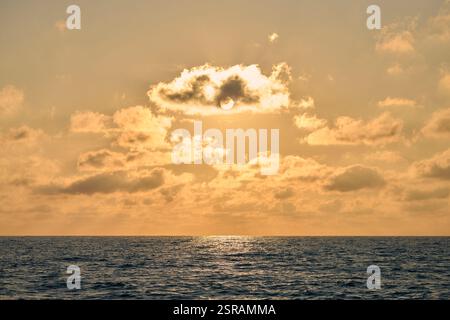 Ein ruhiger goldener Sonnenuntergang strahlt warmes Licht über den friedlichen Horizont des Ozeans und schafft eine ruhige Atmosphäre. Sanfte Sonnenstrahlen durchdringen verstreute Wolken und beschwören Stockfoto