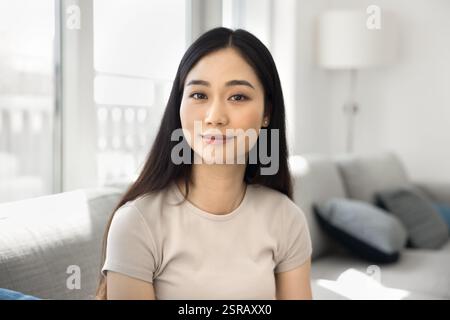 Hübsche asiatische junge Frau, die in einem gemütlichen, gut beleuchteten Zimmer sitzt Stockfoto