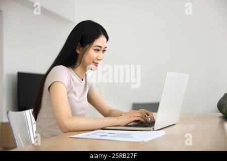Junge asiatische Frau, die am Schreibtisch sitzt und intensiv am Laptop arbeitet Stockfoto