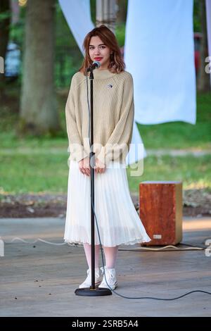 Kaliningrad, Russland - 10.08.2024 - Junge Frau mit Mikrofon singt leidenschaftlich im Park, umgeben von grünem Laub Stockfoto