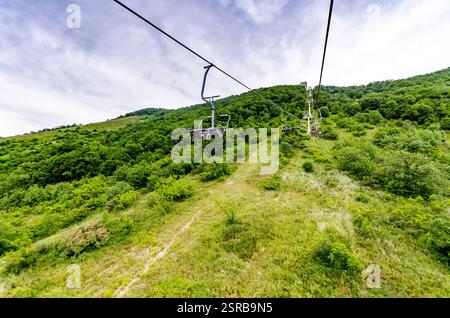 Seilbahn über üppig grünen Wald mit Bergkulisse. Helles Tageslicht sorgt für eine lebendige Landschaft. Abenteuergefühl aus der Perspektive Stockfoto