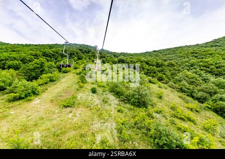 Seilbahn über üppig grünen Wald mit Bergkulisse. Helles Tageslicht sorgt für eine lebendige Landschaft. Abenteuergefühl aus der Perspektive Stockfoto