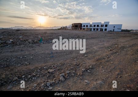 Wüstenhotel im Bau, in warmes Sonnenuntergangslicht getaucht. Raues Gelände umgibt das Gebäude mit verstreuten Wolken, die den Himmel noch tiefer machen. Umfangreich Stockfoto