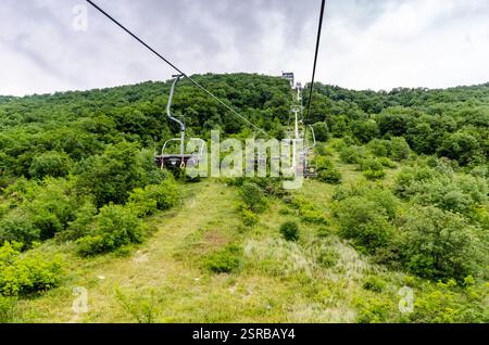 Seilbahn über üppig grünen Wald mit Bergkulisse. Helles Tageslicht sorgt für eine lebendige Landschaft. Abenteuergefühl aus der Perspektive Stockfoto