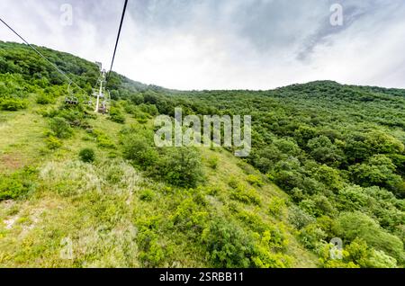 Seilbahn über üppig grünen Wald mit Bergkulisse. Helles Tageslicht sorgt für eine lebendige Landschaft. Abenteuergefühl aus der Perspektive Stockfoto