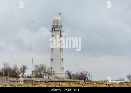Majestätischer Leuchtturm steht hoch an der felsigen Küste unter bewölktem Himmel. Spärliche Vegetation und Antenne in der Nähe schaffen eine ruhige, isolierte Meereslandschaft. Weiches Licht Stockfoto