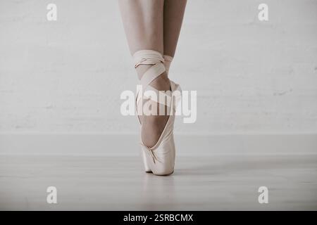 Nahaufnahme junger weiblicher Ballerina mit spitzenschuhen im lichtdurchfluteten Atelier. Sanfte Beleuchtung hebt anmutige Posen und Beigetönen hervor und schafft so ein ruhiges A Stockfoto