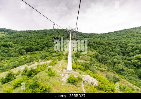 Seilbahn über üppig grünen Wald mit Bergkulisse. Helles Tageslicht sorgt für eine lebendige Landschaft. Abenteuergefühl aus der Perspektive Stockfoto