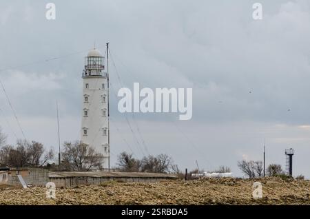 Majestätischer Leuchtturm steht hoch an der felsigen Küste unter bewölktem Himmel. Spärliche Vegetation und Antenne in der Nähe schaffen eine ruhige, isolierte Meereslandschaft. Weiches Licht Stockfoto