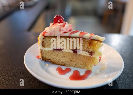 Ein Stück bakewell-Kuchen mit Himbeerauflage auf einem weißen Teller. Der Kuchen wird in zwei Hälften geschnitten und hat einen Hauch Himbeersoße Stockfoto