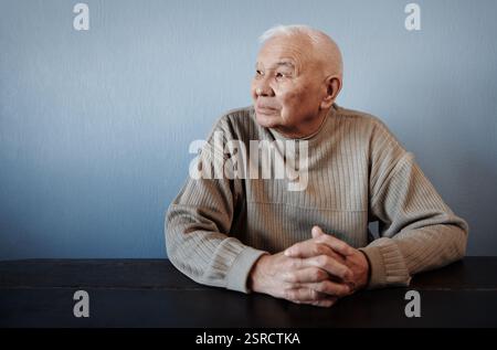 Nachdenklicher und nachdenklicher Seniorenmann, der am Tisch sitzt Stockfoto
