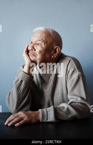 Nachdenklicher und nachdenklicher Seniorenmann, der am Tisch sitzt Stockfoto
