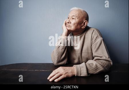 Nachdenklicher und nachdenklicher Seniorenmann, der am Tisch sitzt Stockfoto